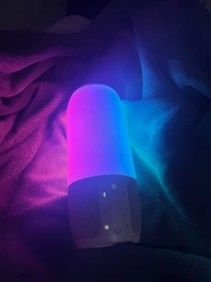 Trådlös jbl högtalare med LED-belysning - Cool trådlös högtalare med färgskiftande LED-ljus som lyser i regnbågens färger. Högtalaren har vit bas, rundad form och tydliga knappar för volym, ljus och Bluetooth. USB-port och AUX-ingång finns. Perfekt för att skapa stämning med både musik och ljus.
