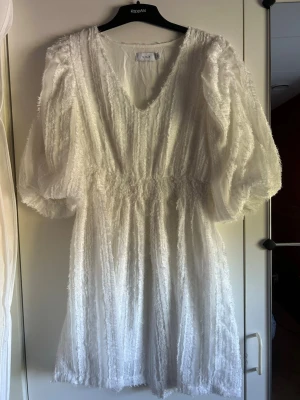 Vit fluffig kortklänning från VILA - Supersöt vit kortklänning från VILA med puffiga trekvartsärmar och v-ringning. Klänningen har en fluffig textur och markerad midja. Perfekt student💗Aldrig använd men prislappen sitter ej kvar! 