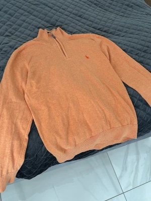 Halvzip Polo Ralph Lauren - Orange halvzip-tröja från Polo Ralph Lauren med hög krage och ribbade muddar vid ärmslut och nederkant. 