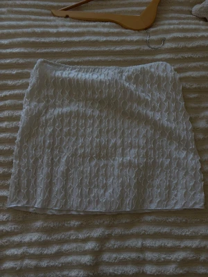Vit kortkjol med strukturmönster - Säljer en vit kortkjol med snyggt strukturmönster och elastisk midja. Kjolen är i ett lätt och bekvämt material.