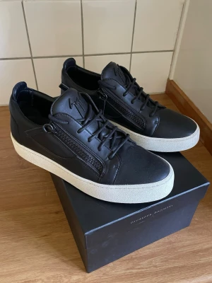 Giuseppe Zanotti - Snygga svarta sneakers i läder från Giuseppe Zanotti med vita tjocka sulor. Skorna har dragkedjor på sidorna, svarta skosnören och diskret logga på plösen. Perfekta för dig som gillar stilrena och exklusiva sneakers med en modern touch.