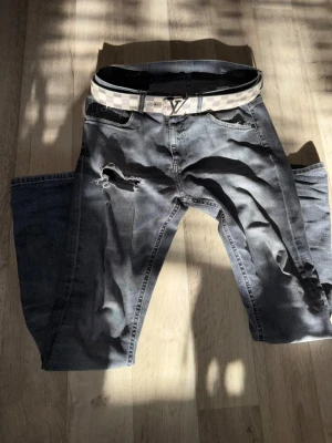 Grå slitna jeans från dondup - Säljer ett par grå jeans med slitningar och hål på ena låret från dondup. Jeansen har klassisk femficksdesign.Perfekt för dig som gillar streetstyle och vill sticka ut. Om du vill ha med bältet kostar de 50 kr extra. De finns några problem i jeansen som inte syns utifrån så skriv till mig och jag säger till!