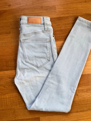 Ljusblå skinny jeans från Bikbok - Säljer ett par ljusblå skinny jeans från Bikbok med klassisk femficksdesign och hög midja. Jeansen är i stretchigt denimtyg och har en snygg, smal passform som sitter tajt hela vägen ner. Perfekta för en avslappnad och trendig look.