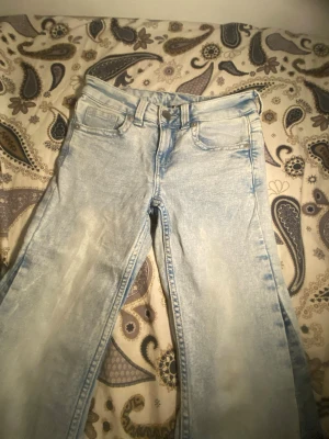 Ljusblå bootcut jeans H&M  - Säljer ett par ljusblå jeans med utsvängda ben och klassisk femficksdesign. Jeansen har en tvättad look och är gjorda i denim. Perfekta för dig som gillar retro och avslappnad stil.