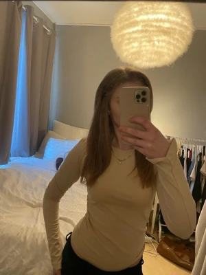 Beige långärmad topp - Säljer en stilren beige långärmad topp med rund halsringning. Toppen har en slim passform och är perfekt att matcha med jeans eller kjol. Materialet känns mjukt och stretchigt, vilket gör den bekväm att bära hela dagen.