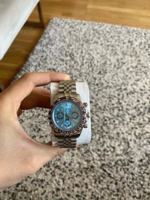 Seiko kronografklocka med blå urtavla - Stilren Seiko kronografklocka med ljusblå urtavla och silverfärgad länk i metall. Klockan har en brun bezel med tachymeterskala och flera små urtavlor för extra funktioner. Perfekt accessoar för dig som gillar sportig och modern stil.