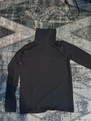 Svart turtleneck från Name It - Svart långärmad turtleneck från Name It, tillverkad i mjuk ekologisk bomull. Enkel och stilren design som passar perfekt till lager-på-lager eller som den är. Polokragen ger extra värme och en clean look.
