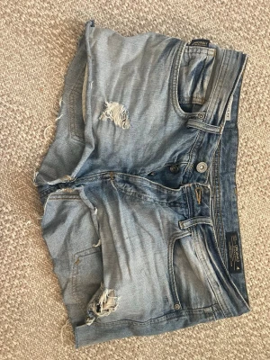 Blå slitna jeansshorts  - Säljer ett par jätte snygga shorts från Jack & Jones🌸 Sitter lite mid/low skulle jag säga köpta med slitningar så de ska vara så💗 Har också lite smuts på sig kommer tvätta de också ifall nån köper!!