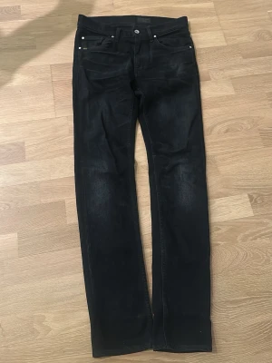 Svarta raka jeans - Snygga svarta jeans från tiger of sweden med rak passform och klassisk femficksdesign. Jeansen har silverfärgade nitar och knapp, samt en diskret läderpatch bak i midjan. Perfekta till en avslappnad streetstyle-look.