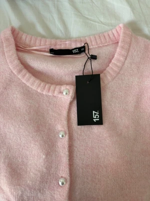 Ljusrosa kofta från 157 - Supersöt ljusrosa kofta från 157 med rund halsringning och korta ärmar. Koftan har pärlknappar framtill och är stickad i ett mjukt material. Tröjan har även kvar lappen och är oanvänd! Pris går att diskutera och jag kan skicka klädsplaggst snabbt! 💕