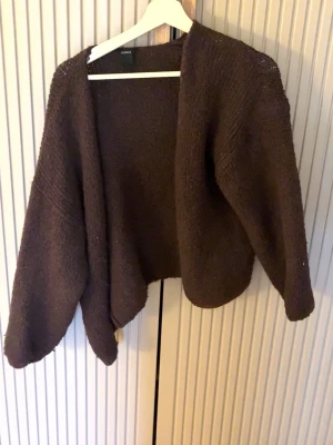 Vinröd stickad kofta från Lindex - Mysig vinröd/brun stickad kofta från Lindex med öppen front och avslappnad passform. Perfekt att slänga över en t-shirt eller topp för extra värme. Koftan har långa ärmar och är gjord i ett mjukt, grovstickat material. Dock är den lite nopprig. Storleken är borttvättad men skulle säga S.