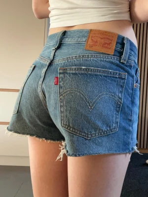 Levi's blå jeansshorts med rå kant - Säljer ett par klassiska blå jeansshorts från Levi's med midwaist. Står ingen storlek men för referens är jag 165 vm och väger ca 53 kg och de sitter rätt löst på mig💕