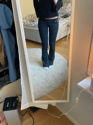 Coola low waist bootcut jeans i svart med grön tvätt! - Säljer ett par svarta bootcut jeans med låg midja. Jeansen har klassisk femficksdesign och stängs med knapp och dragkedja. Snygg passform som sitter tight upptill och släpper ut vid benen. Perfekta till en trendig och avslappnad look.