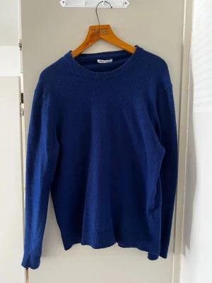 Mörkblå stickad tröja - En enkel och stilren mörkblå stickad tröja med rund halsringning och långa ärmar. Tröjan har ribbade muddar vid ärmslut och nederkant. Perfekt att matcha med jeans eller kjol för en avslappnad look.