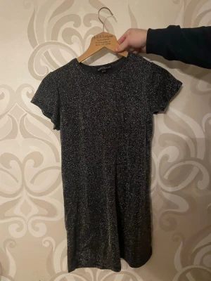 Svart glittrig kortklänning - svart klänning med glittrigt tyg. Klänningen har korta ärmar och en rak passform som ger en enkel men snygg look. Perfekt för tex nyår eller nå kalas