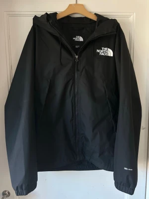 Svart regnjacka från The North Face - Helt ny svart regnjacka från The North Face med dragkedja framtill, huva och logga på bröstet. Tillverkad i ett lätt och vattenavvisande material, perfekt för regniga dagar. Använd 2 gånger totalt, säljer den för att den är för stor.