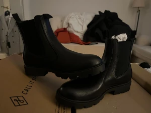 Svarta Chelsea boots från Call It Spring - Säljer ett par svarta Chelsea boots från Call It Spring. Boots i slätt, matt konstläder med elastiska resårpaneler på sidorna och grov sula. Klassisk siluett med dragflik bak för enkel påtagning. Perfekta för en stilren och modern look.