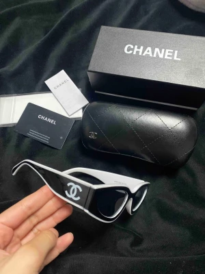 Svarta/vita solglasögon  - Snygga solglasögon med svart och vit båge och tydlig logga på sidorna. Glasögonen har en unik, futuristisk form och levereras med originalfodral och sådant. Perfekt accessoar för dig som vill sticka ut med en lyxig vibe.