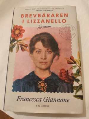 Brevbäraren i Lizzanello - Romanen 'Brevbäraren i Lizzanello' av Francesca Giannone är en familjesaga som utspelar sig i Italien 1934. Omslaget har en vintageinspirerad design med blommor och porträtt, tryckt i mjuka färger. Boken är inbunden och texten är på svenska.