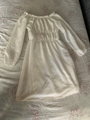Vit offshoulder kortklänning - Söt vit kortklänning med offshoulder och långa ärmar. Klänningen har resår i midjan och runt axlarna samt diskret prickigt mönster i tyget. Perfekt för sommarens alla tillfällen och ger en romantisk vibe.