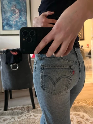 Low waist bootcut jeans - Säljer ett par klassiska ljusblå Levi's jeans med bootcut passform. Jeansen har fem fickor, normal midja och den ikoniska röda Levi's-lappen på bakfickan. Tillverkade i slitstark denim med snygg tvätt och subtila slitningar. Perfekta för en avslappnad och trendig look.