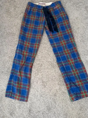 vintage Blårutiga pyjamasbyxor Hollister - Säljer ett par blårutiga pyjamasbyxor från Hollister med klassiskt rutmönster i blått, rött, grönt och gult. Byxorna har resår i midjan, mörkblå knytband och en broderad Hollister-logga vid fickan. Perfekta för mysiga hemmakvällar. Storlek S pris kan diskuteras
