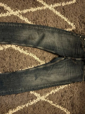 Mörkblå Tiger of Sweden jeans - Snygga mörkblå jeans från Tiger of Sweden med klassisk femficksmodell och raka ben. Jeansen har slitningar och kontrastsömmar samt en patch med logga bak i midjan. Perfekta till en avslappnad stil och tillverkade i mjukt denimtyg.