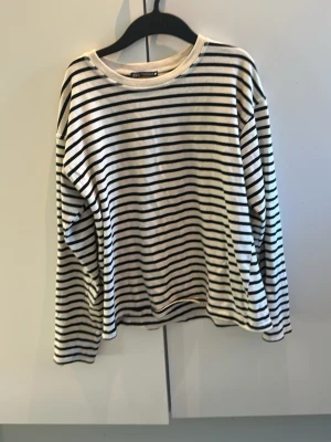 Randig långärmad tröja Zara - Säljer en vit långärmad tröja från Zara med tunna svarta horisontella ränder. Tröjan har rund halsringning och är gjord i mjukt bomullsmaterial. Perfekt för en avslappnad och stilren look och nu till sommaren!! Knappt använd💕