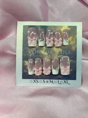 BlushBow (M);Medium Square - Handgjorda press-on naglar i en mjuk nuderosa och vit handmålad french med 3D rosa rosetter och pärlhjärtan. Naglarna har en elegant, medium lång square form och är perfekta för dig som vill ha en söt och trendig look. M: 16 mm, 12 mm, 12,5 mm, 11,5 mm, 10 mm, och designen är detaljerad och unik.