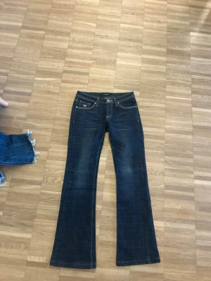 Mörkblå bootcut jeans med brodyr - Säljer ett par mörkblå bootcut jeans med snygga broderade detaljer på bakfickorna. Jeansen har låg midja. Dragkedjan är trasig men går att fixa. Priset kan diskuteras!