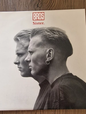 Bros Sister vinylsingel - Vinylsingel med omslag i svartvitt från bandet Bros, låten 'Sister'. Omslaget har ett porträtt i profil och text i rött. Baksidan är turkos med låtinfo och credits. Perfekt för dig som gillar 80-talsmusik och samlar på vinyl.