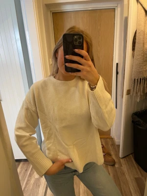 Krämvit stickad tröja - Mysig krämvit stickad tröja med rund halsringning och ribbade muddar vid ärmslut och nederkant. Tröjan har en avslappnad passform och är perfekt att matcha med jeans för en enkel och stilren look.