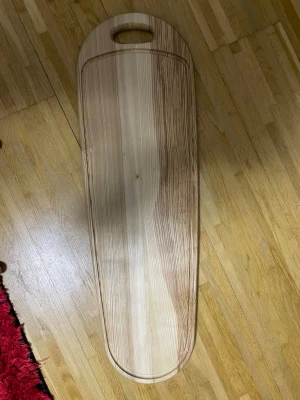 Stor träbricka från Herolux - Säljer en stor, avlång träbricka från Herolux med naturlig träfärg och ett praktiskt handtag. Perfekt för servering eller som dekoration. Tillverkad i Finland och har en snygg ådring i träet som ger en unik look.