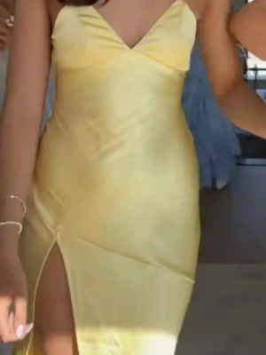 Gul långklänning med snörning - Snygg gul långklänning i satin material med smala axelband som korsas och knyts i ryggen. Klänningen har en hög slits framtill och öppen rygg, vilket ger en elegant och trendig look. Perfekt för balen❤️aldrig använt