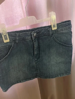 Blå jeanskjol i kort modell - Säljer en klassisk blå jeanskjol i kort modell med fem fickor och knappgylf. Kjolen har en enkel, tidlös design och passar perfekt till en avslappnad stil. Tillverkad i denim med snygga sömdetaljer. Jag har strl xs men den passar bra!