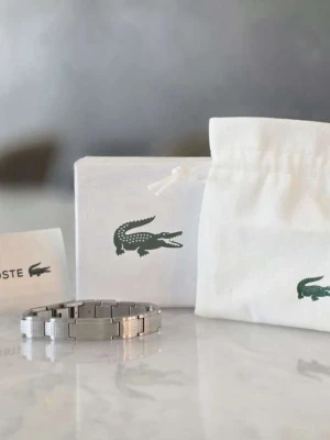Silverfärgad klocka från Lacoste - Stilren klocka från Lacoste i silverfärgat metallarmband. Klassisk design med diskret logga och länkarmband. Perfekt accessoar för dig som gillar en clean och tidlös look.