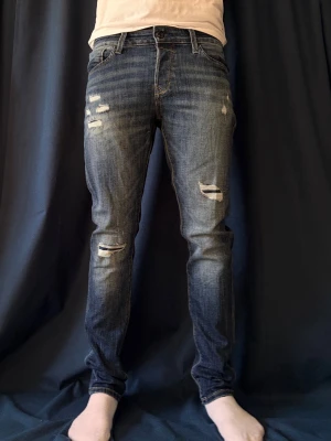 Jack and jones jeans - Säljer ett par blå slim fit jeans med slitningar från jack and jones. Jeansen har klassisk femficksdesign, normalhög midja och dragkedjegylf. Perfekta för en avslappnad och trendig look. Öppen för prisförslag!