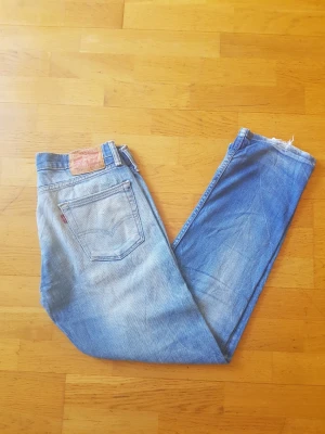 Levi's 513 ljusblå jeans - Säljer ett par klassiska Levi's 513 jeans i ljusblå tvätt med raka ben och hög midja. Jeansen har fem fickor, läderpatch bak och rå kant vid benslutet för en trendig look. Tillverkade i bomull för skön känsla och slitstark kvalitet.