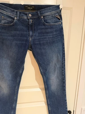 Blå jeans från Replay med smal passform - Storlek S,  Snygga blå jeans från Replay med klassisk femficksmodell och smal passform. Jeansen har en lätt tvättad look med subtila slitningar och detaljerade sömmar. Tillverkade i stretchigt denim för extra komfort och rörelsefrihet.
