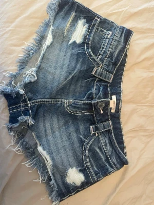 Blå jeansshorts - Blåa jeansshorts med slitna detaljer och fransig kant. Perfekta för varma dagar och ger en avslappnad vibe. Köpta på Gina young💗
