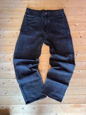 Svarta jeans - Säljer ett par svarta Weekday Galaxy Loose Straight Jeans med rak och lös passform. Jeansen har klassisk femficksdesign och är tillverkade i bomull. Perfekta för en avslappnad och trendig stil.