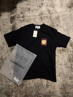 Svart t-shirt från Casablanca - Svart t-shirt från Casablanca med färgglatt tryck på bröstet som föreställer en svamp och texten 'Casa Blanca'. Klassisk passform med rund hals och korta ärmar. Tillverkad i mjuk bomull, perfekt för en trendig och avslappnad stil.