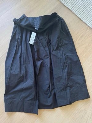 Svart poplinkjol så lång från Gina Tricot - Stilren svart långkjol i poplin från Gina Tricot. Kjolen har en vid och luftig passform med resår i midjan för extra komfort. Perfekt att styla med både sneakers och boots för en trendig look. Jag rekommenderar storlek M