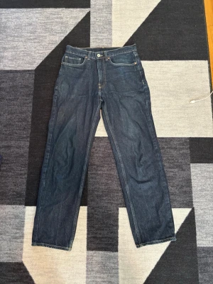 Loose fit jeans från Valeni blå W29 L30 - Säljer ett par blå loose fit jeans från Valeni med klassisk femficksdesign och ljusbruna sömmar. Jeansen har en snygg läderpatch med logga bak i midjan och är tillverkade i slitstark denim. Perfekta för en avslappnad och trendig look.