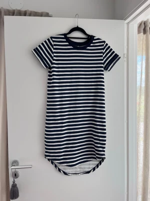 Randig t-shirtklänning från JDY - Säljer en kort t-shirtklänning från JDY i marinblått och vitt med klassiskt randigt mönster. Klänningen har rund halsringning och korta ärmar, tillverkad i mjuk bomull. Perfekt för en avslappnad och stilren look.