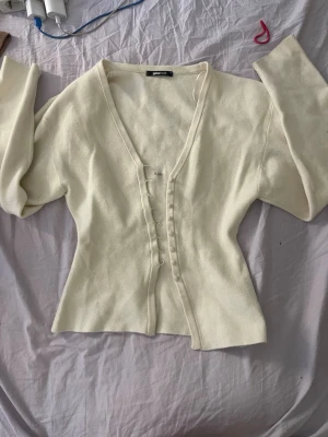 Vit kofta från Gina Tricot XS - Snygg vit kofta från Gina Tricot i storlek XS. Koftan har djup V-ringning, långa ärmar och knäppning framtill med små tygklädda knappar. Mjuk och stretchig kvalitet som sitter figurnära och ger en clean look.
