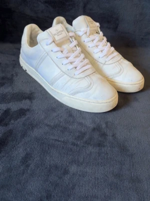 Vita Valentino flycrews - Snygga vita sneakers från Valentino Garavani med klassisk låg profil och vita skosnören. Tillverkade i läder med diskreta detaljer och logotyp på plösen. På ens skon saknas de 3 nitar, men det går enkelt och billigt att köpa nya om man skulle vilja 