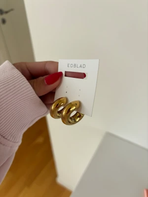 Guldiga chunky örhängen från Edblad - Snygga chunky örhängen i guldton från Edblad. De har en rund, tjock form och är tillverkade i metall med en blank finish. Perfekta för att ge din look en trendig touch. aldrig använda. nypris 449