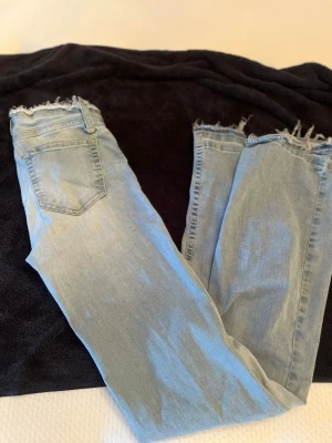 Ljusblå jeans med rå kant från Nelly  - Säljer dessa bootcut jeansen från Nelly. Bra skick förutom att ena flärpen har lossnat på byxorna.