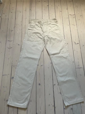 Beige raka chinos från sweet sktbs - Snygga beige chinos från sweet sktbs med rak passform och klassisk design. Byxorna har bälteshällor, knapp och dragkedja framtill samt två bakfickor. Perfekta för en clean och stilren look. Tillverkade i ett slitstarkt bomullsmaterial.